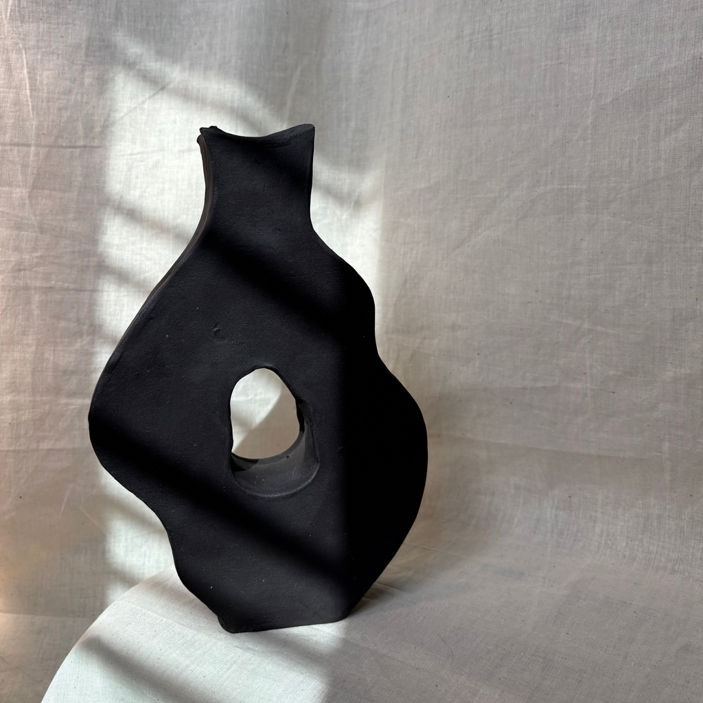 Black abstract sculptural vase on a textured white surface