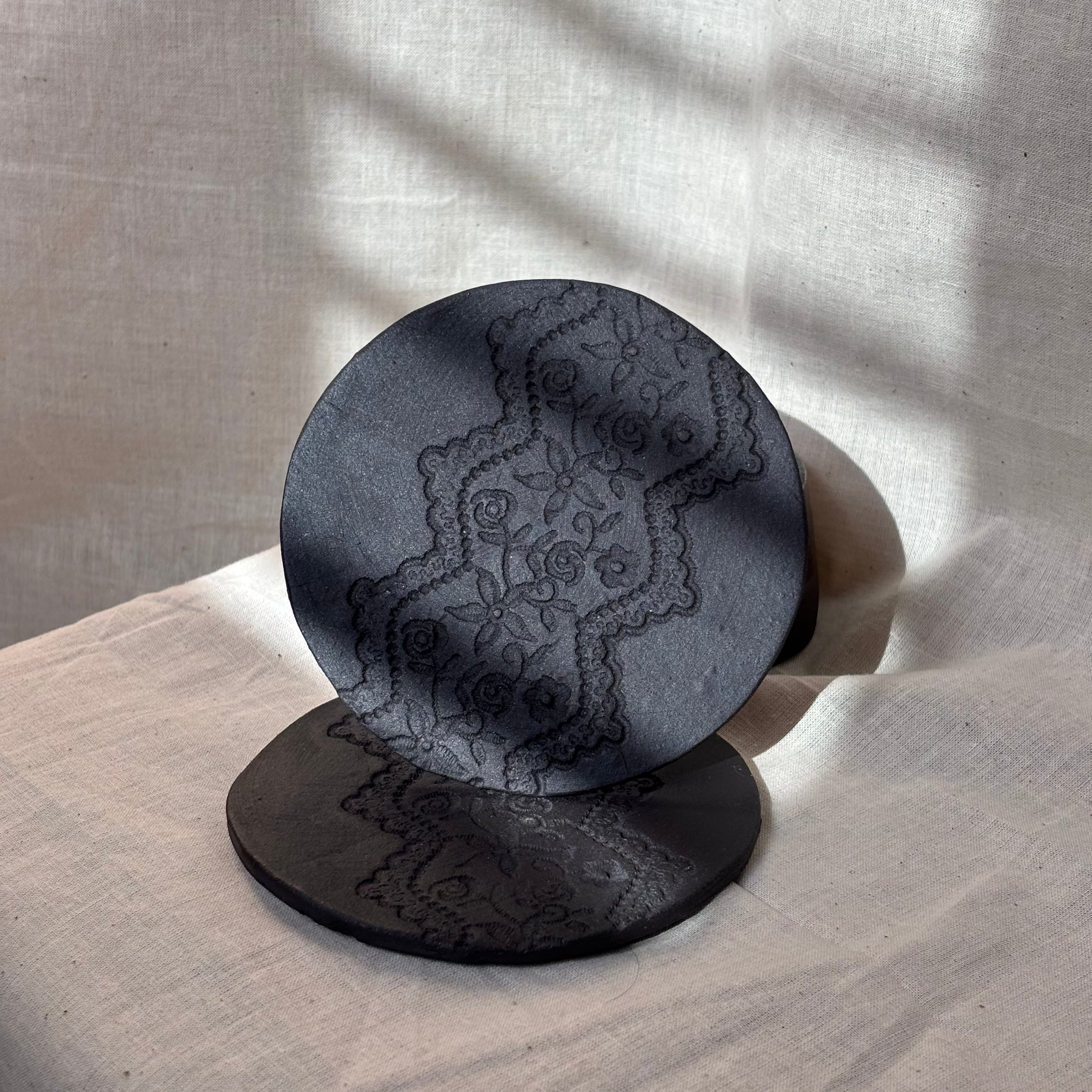 black clay coaster with a lace imprint, unglazed
