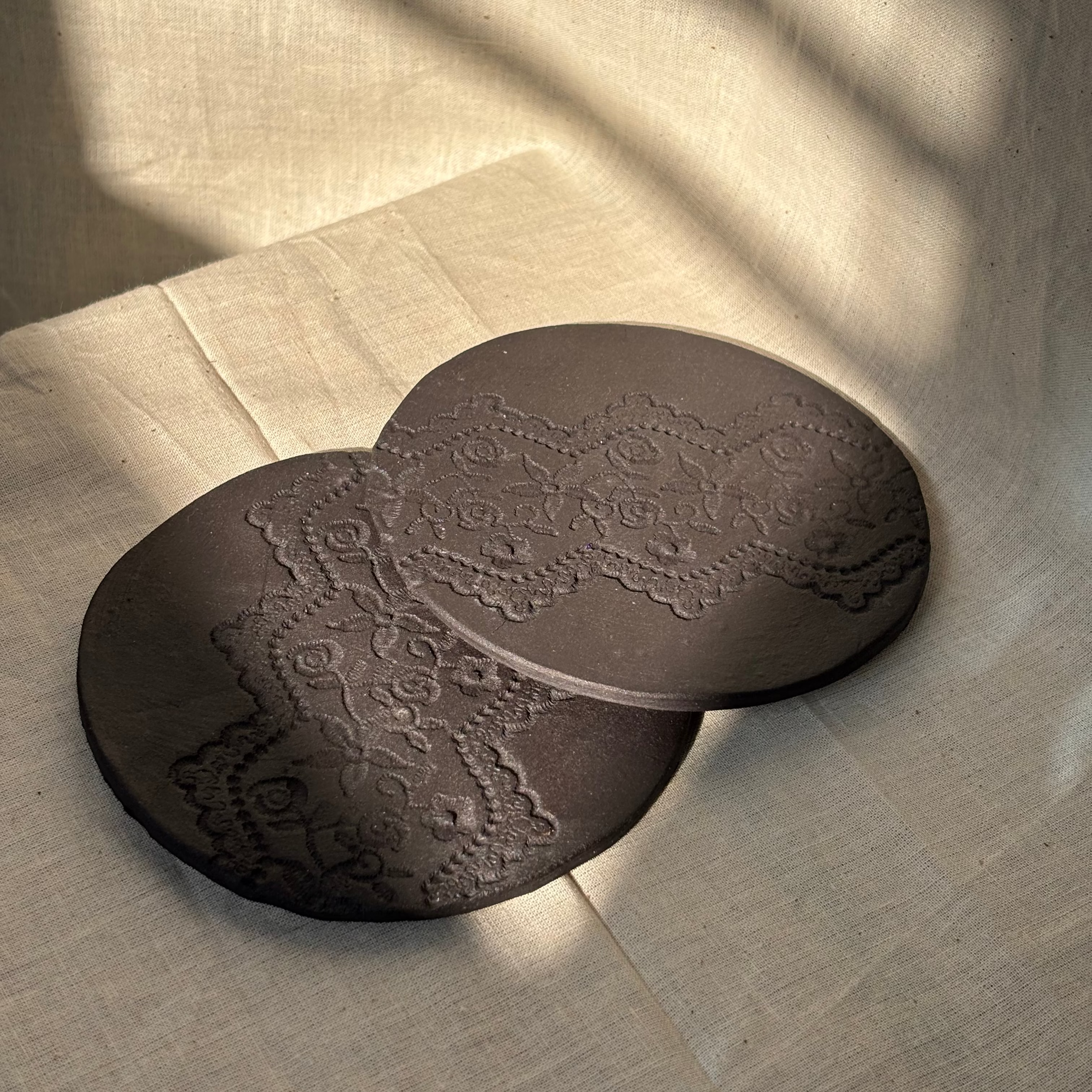 Two black round coasters with intricate patterns on a matte surface.