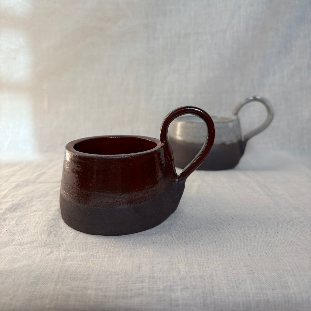 two ceramic candle holders, each half glazed on black clay, one red and one white