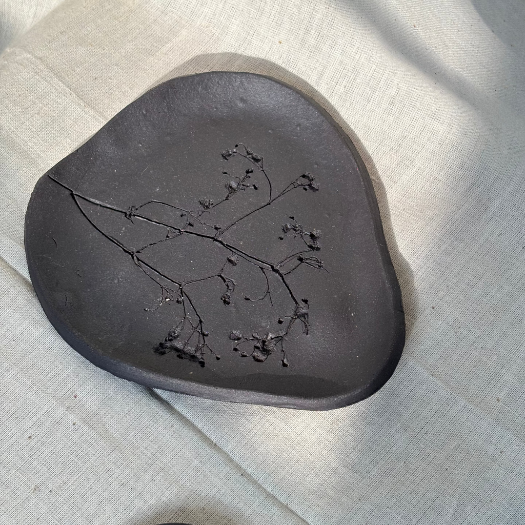 Black ceramic plate with embossed floral design on a textured beige surface