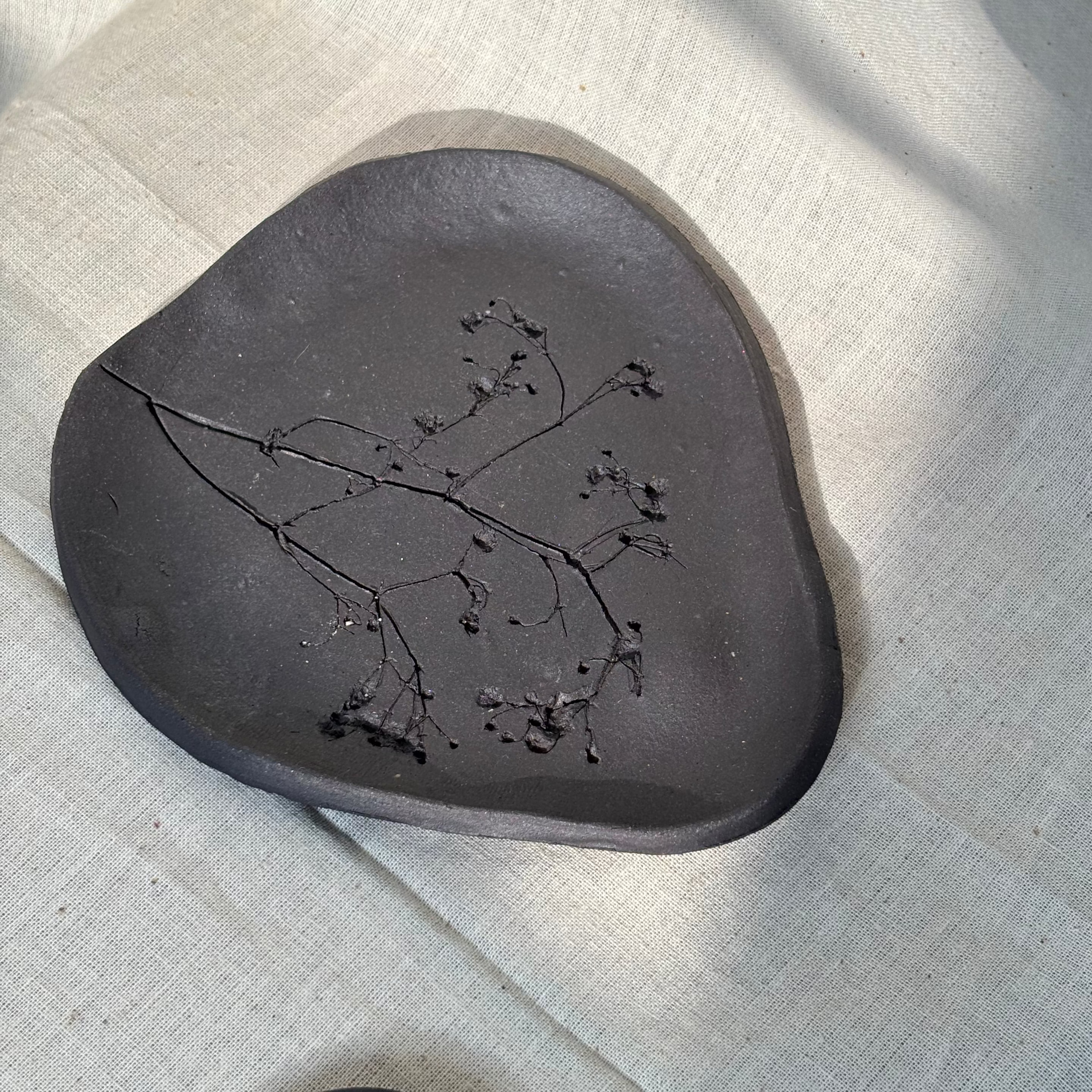 Black ceramic plate with embossed floral design on a textured beige surface