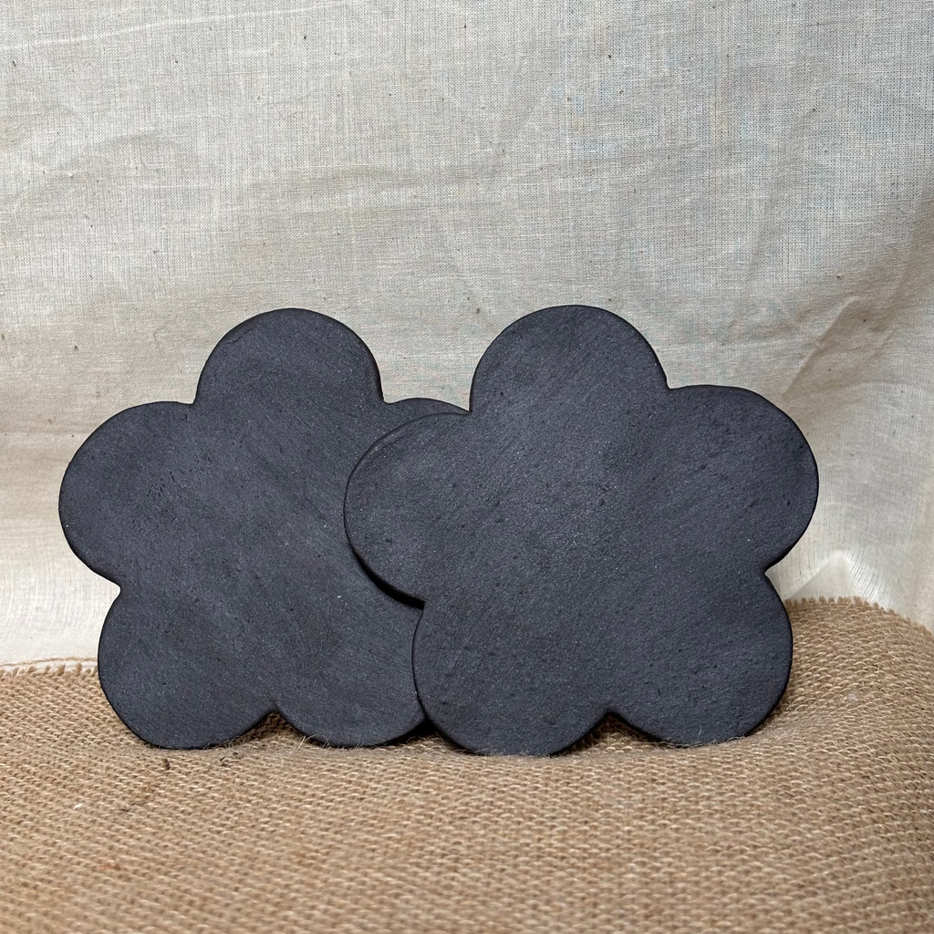 Two black flower-shaped coasters on a textured beige surface with a light gray background