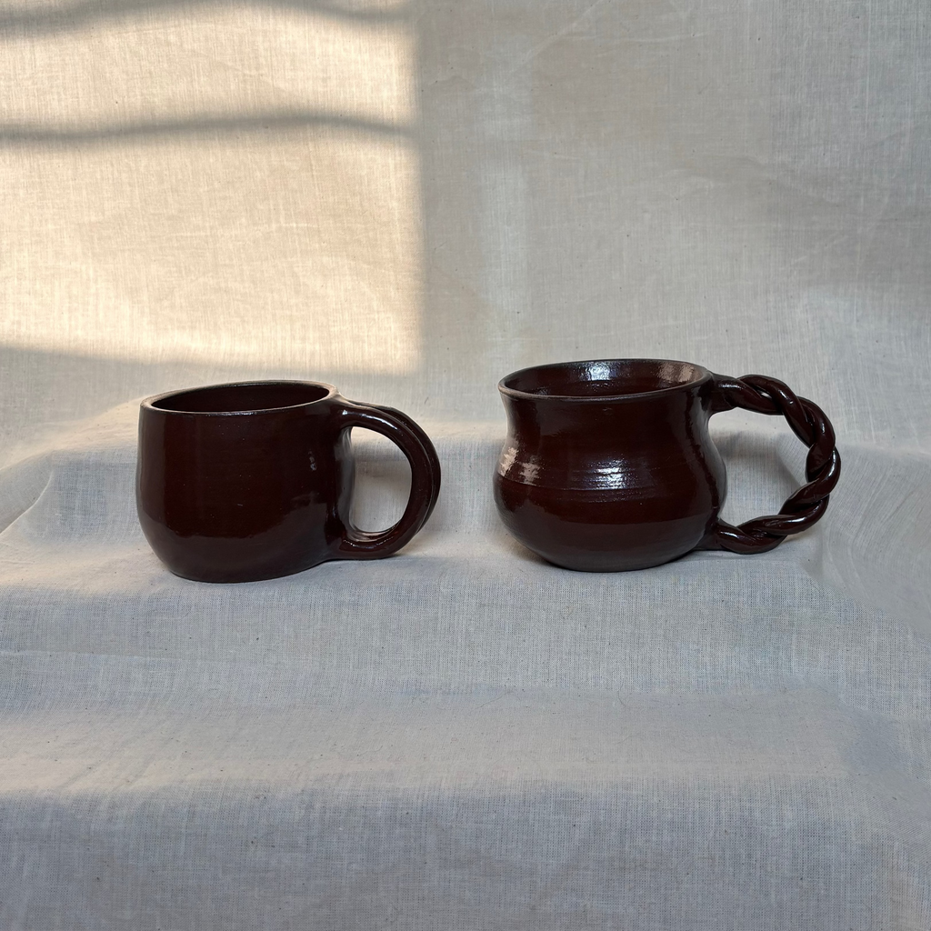 Two deep red ceramic mugs on a textured surface with a neutral background