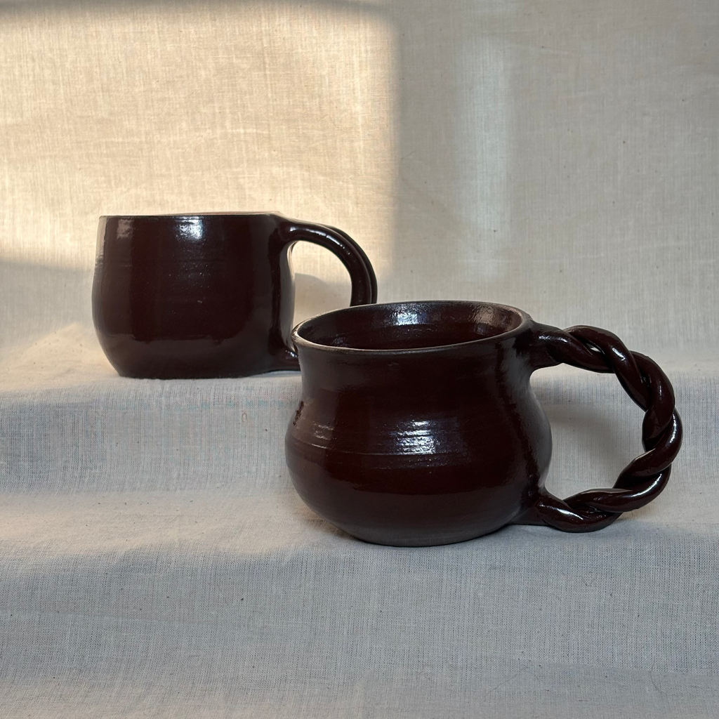 Two deep red ceramic mugs on a textured surface with a neutral background