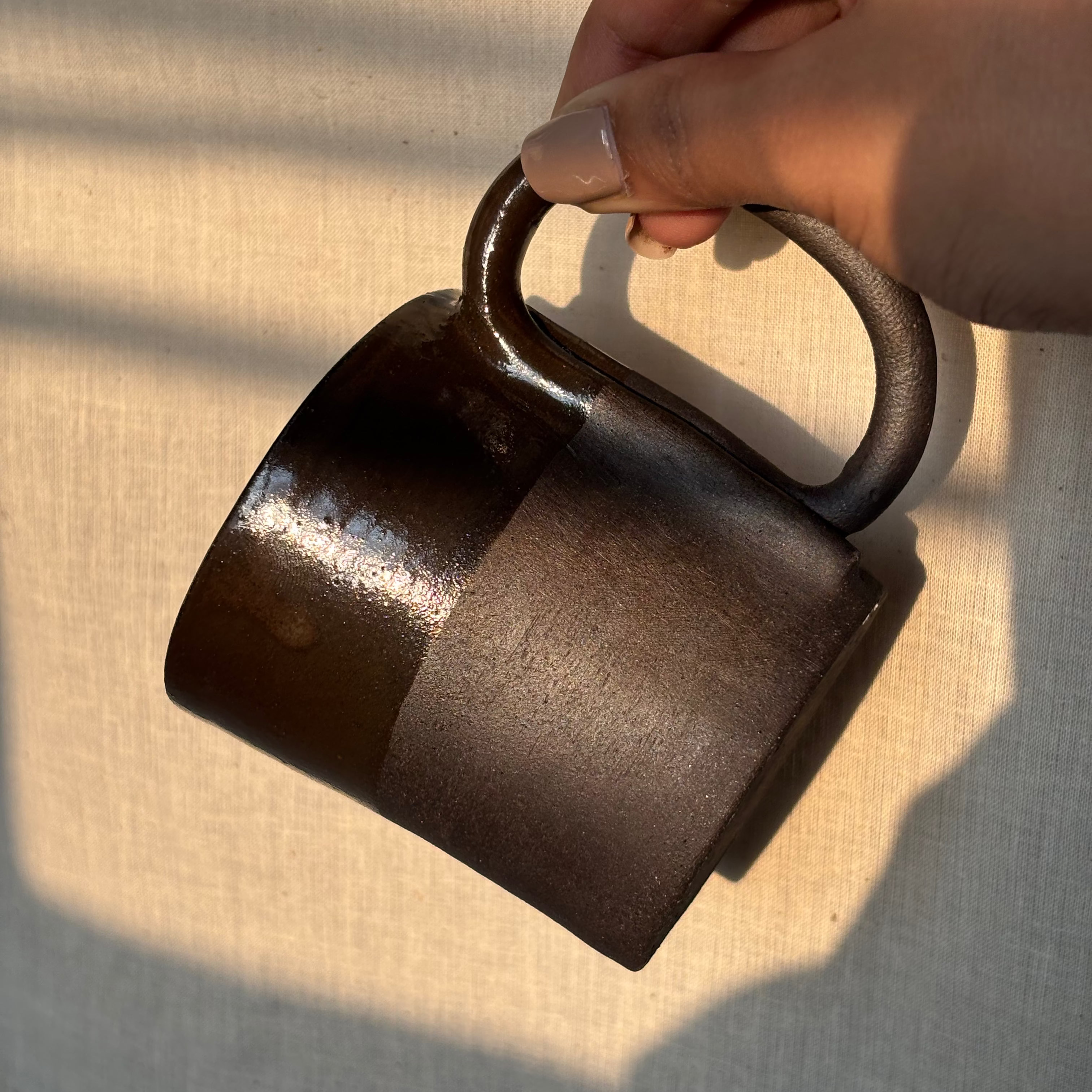 Hand holding a back ceramic mug from the handle against a beige background