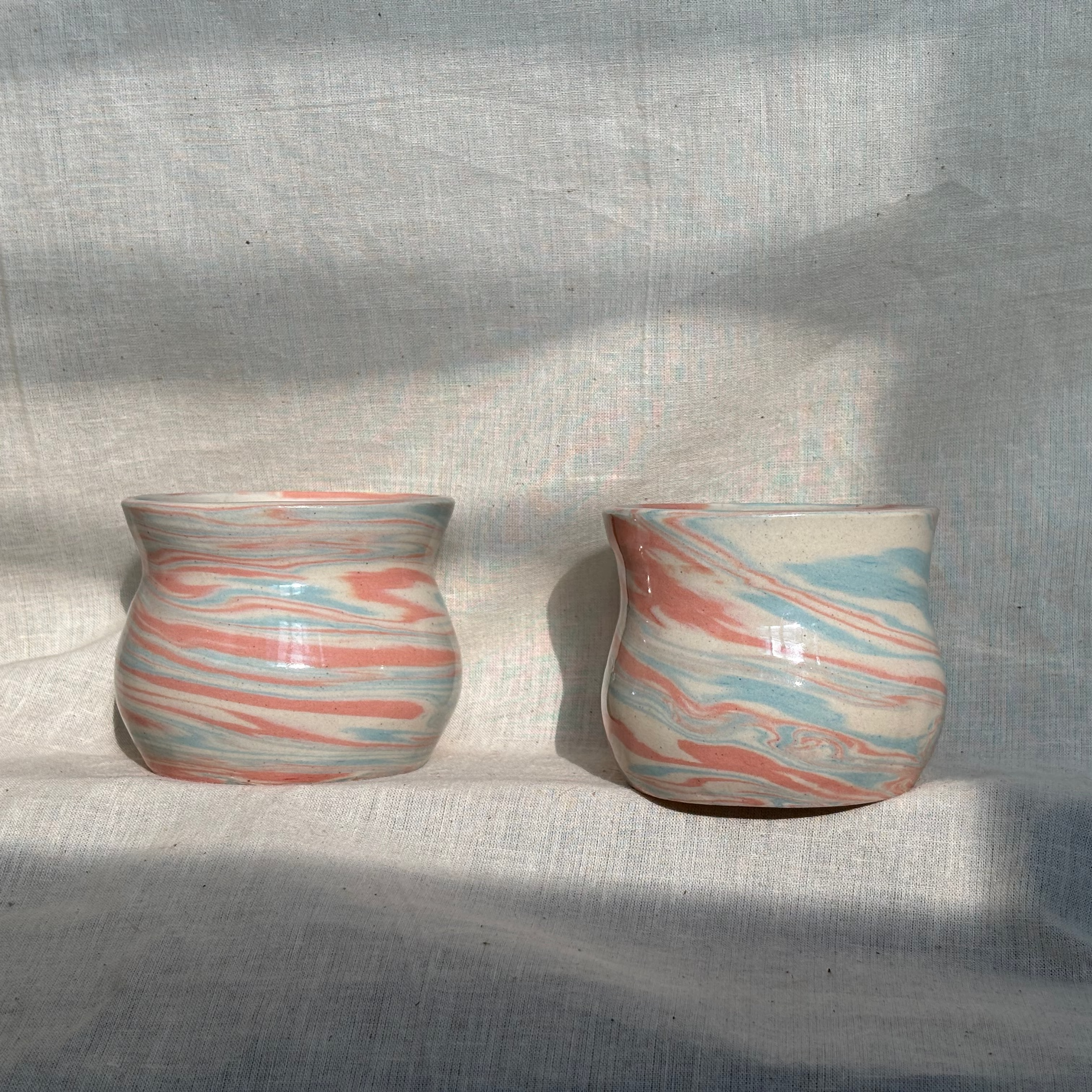Two ceramic cups with marbled design on a textured fabric background