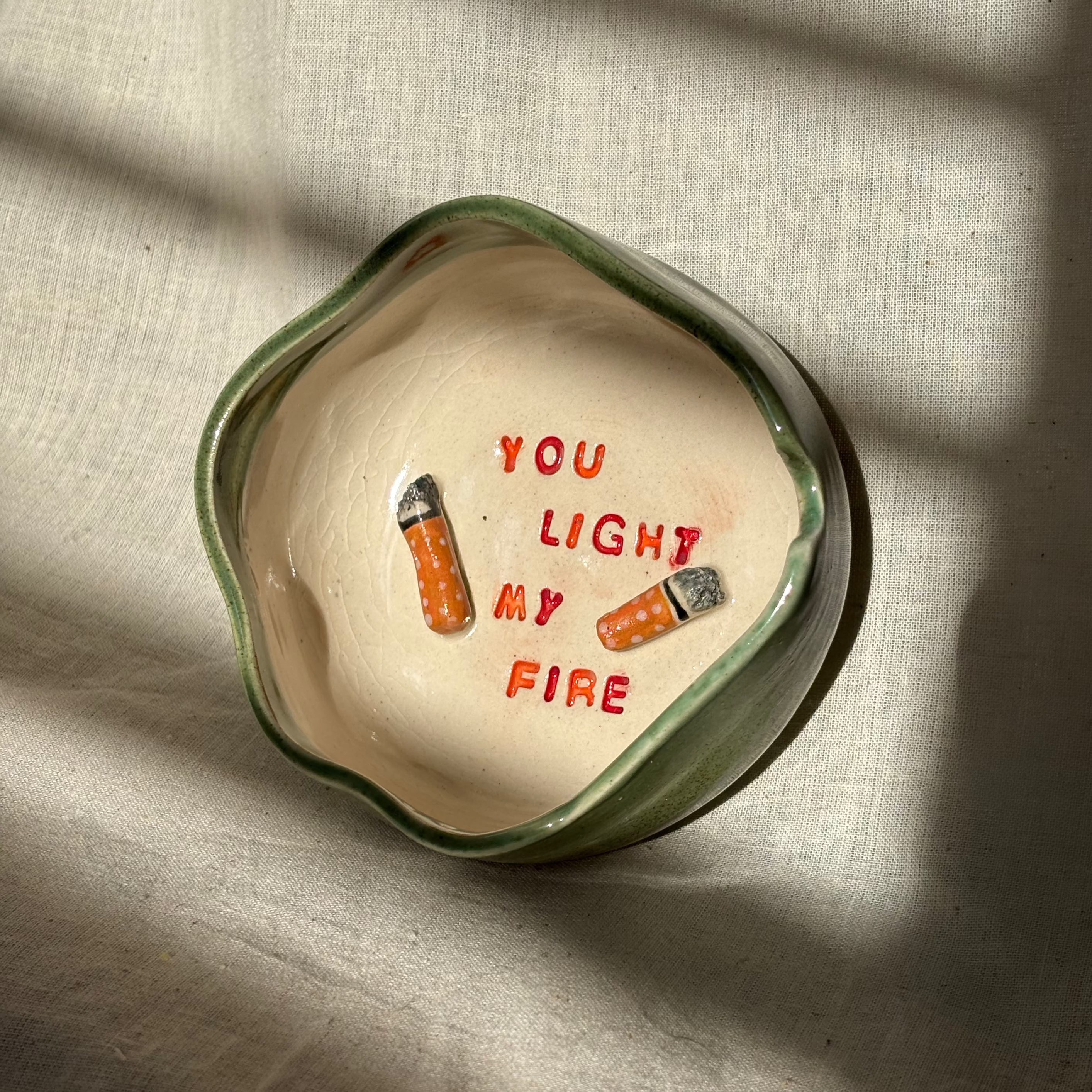 Ceramic ashtray with 'You Light My Fire' text and designs on a textured surface
