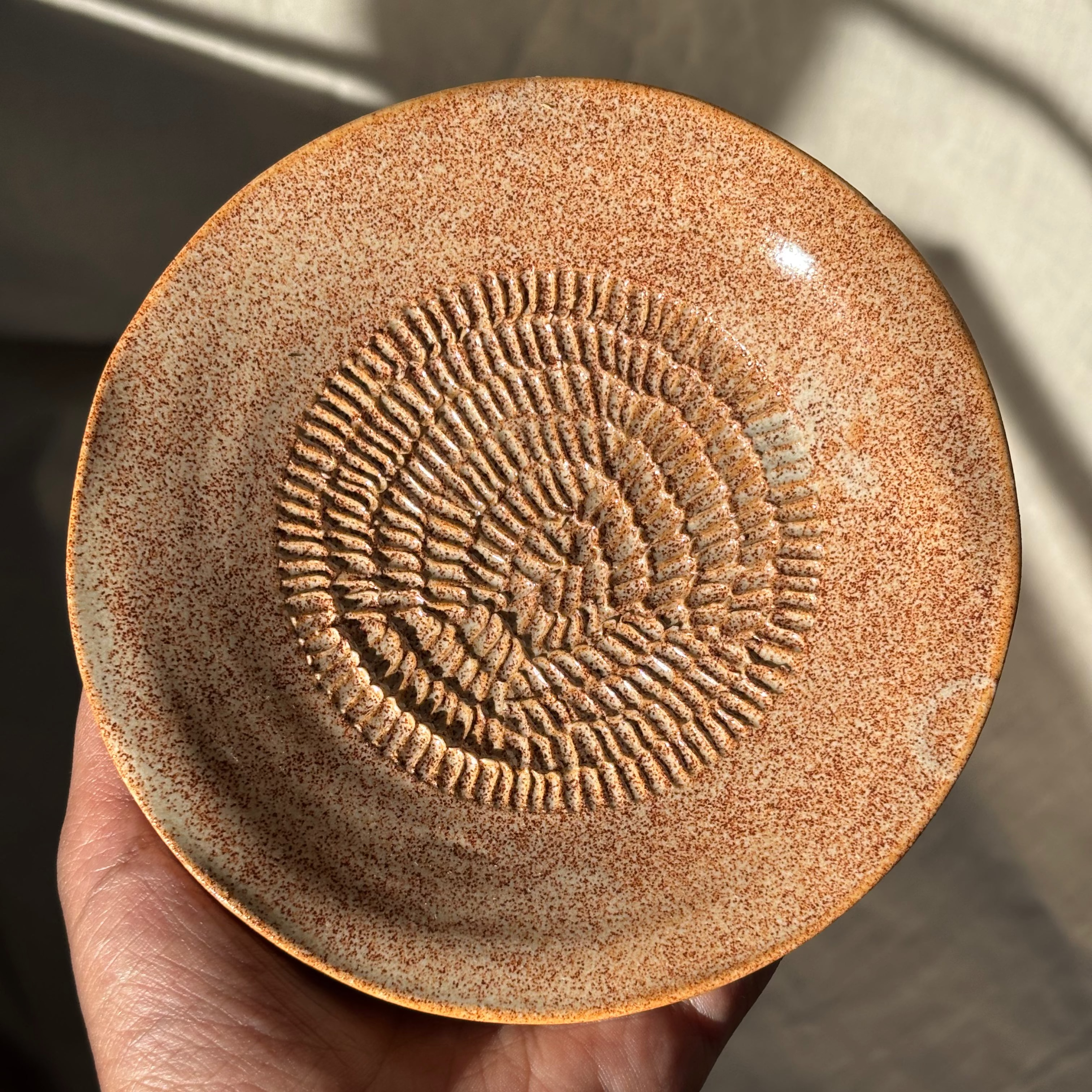 Ceramic dish with textured design in the middle held by a hand against a neutral background
