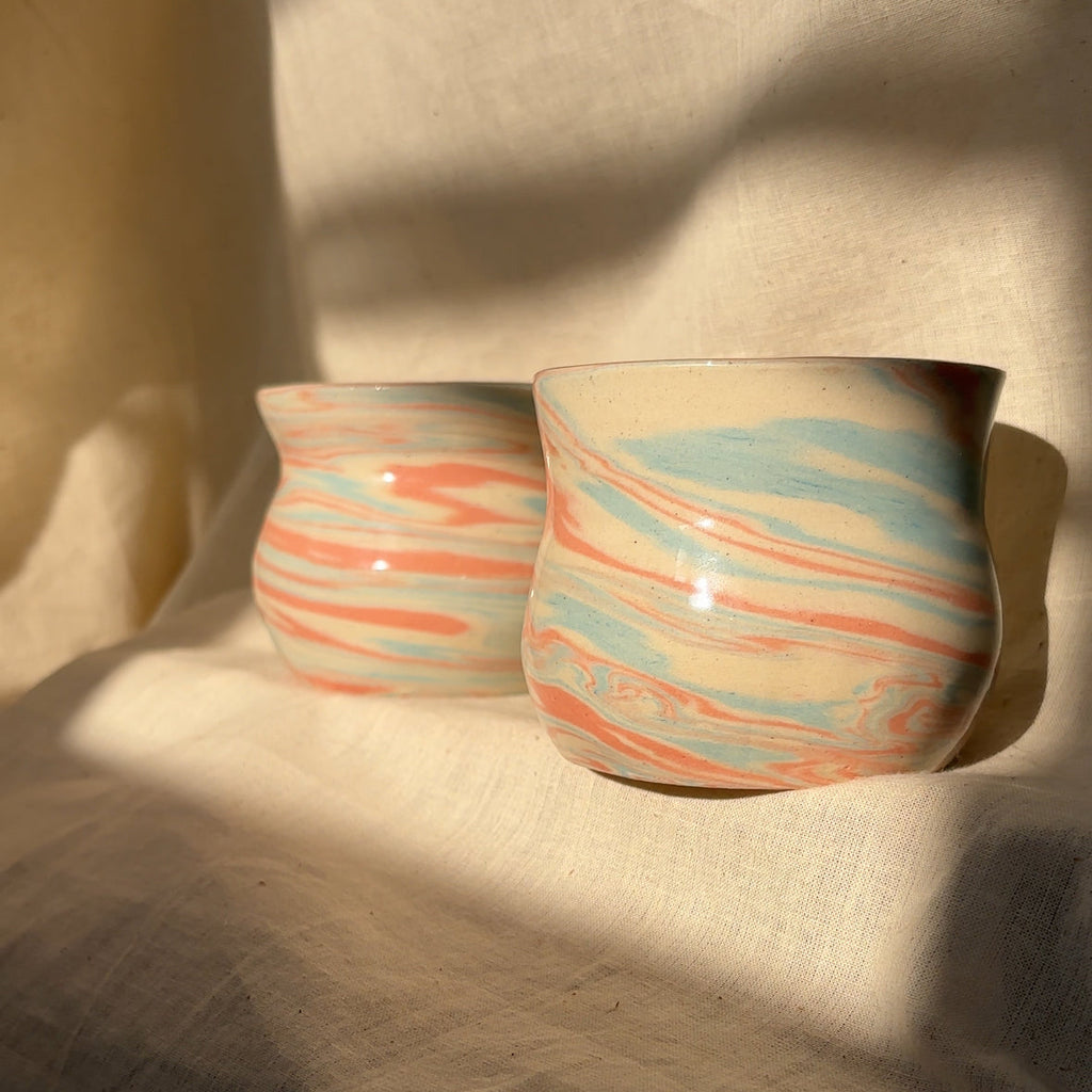 Two ceramic cups with marbled design on a beige fabric background